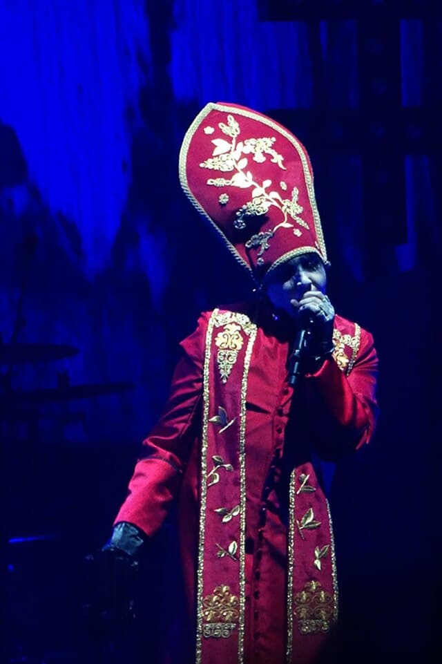 Marilyn Manson performing live during his Holy Wood era tour wearing a striking red priest outfit, symbolizing the fusion of religion and rebellion in his stage persona.