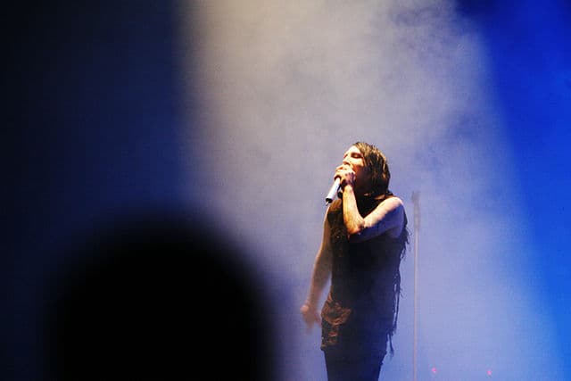 Marilyn Manson performing onstage under a spotlight during a live concert, symbolizing his ongoing influence in 2025.