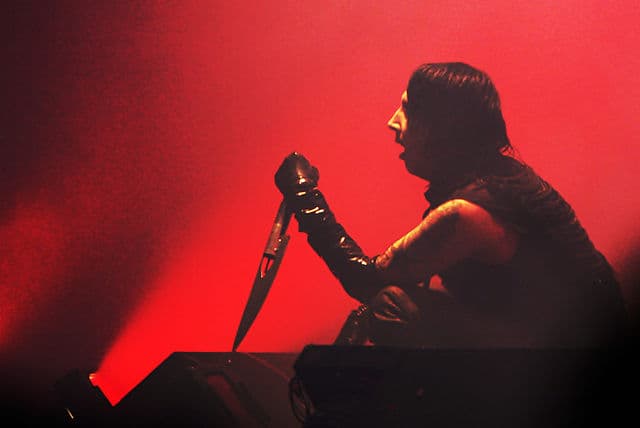 Marilyn Manson performing live under stage lights, showcasing his ever-evolving theatrical persona