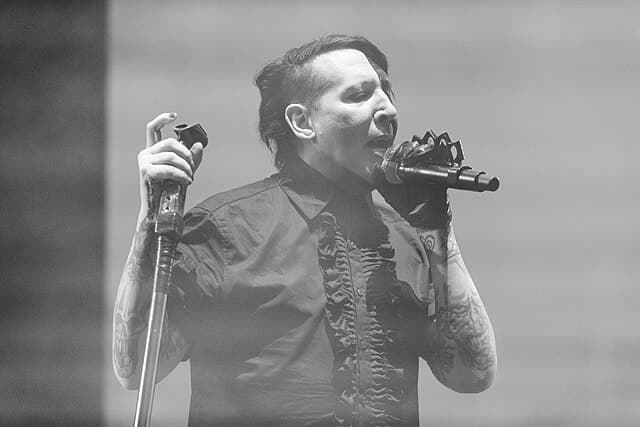 Marilyn Manson performing live on stage wearing an elegant black gothic outfit, showcasing his evolution from shock rock to high fashion.